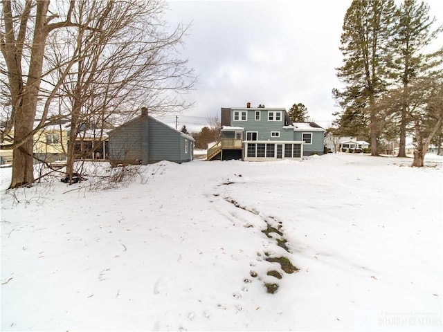 snow covered back of property with a sunroom