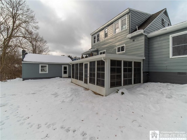 snow covered back of property featuring a sunroom