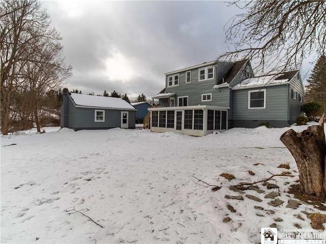 snow covered back of property featuring a sunroom