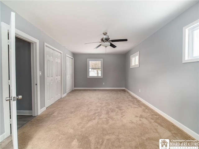 unfurnished bedroom featuring light carpet, two closets, and ceiling fan