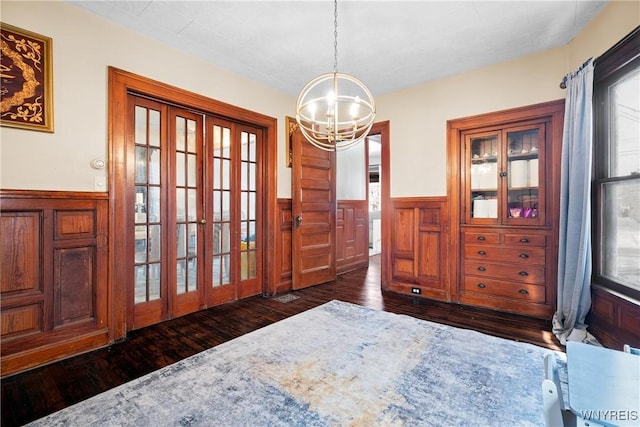 dining space with dark wood-type flooring, an inviting chandelier, and french doors