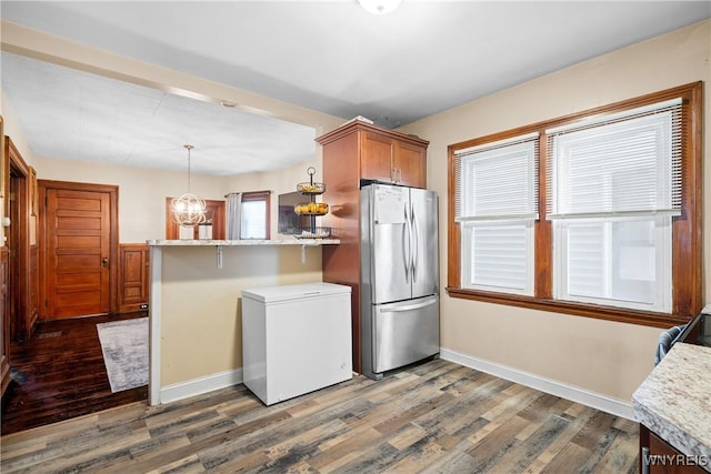 kitchen featuring refrigerator, stainless steel refrigerator, hanging light fixtures, kitchen peninsula, and dark wood-type flooring