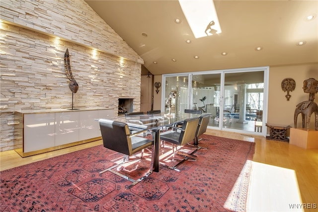 dining space with lofted ceiling, a stone fireplace, and light hardwood / wood-style floors