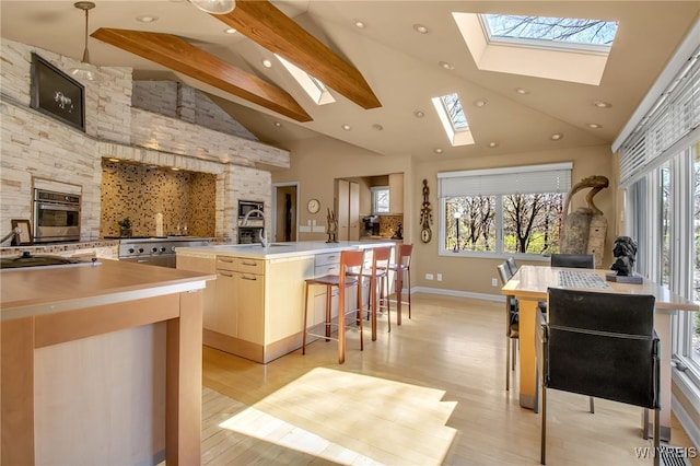 kitchen with sink, a kitchen island with sink, a kitchen bar, decorative light fixtures, and light wood-type flooring