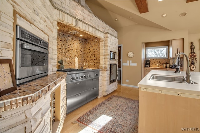 kitchen with lofted ceiling, appliances with stainless steel finishes, sink, and light wood-type flooring