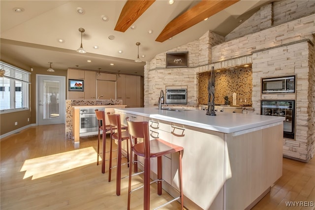 kitchen featuring a large island with sink, light hardwood / wood-style flooring, stainless steel oven, and beamed ceiling