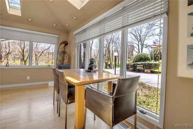 dining space featuring lofted ceiling with skylight and light hardwood / wood-style flooring