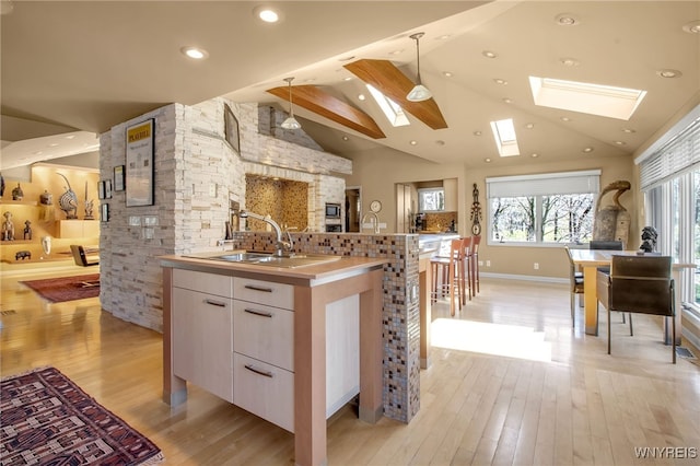 kitchen featuring pendant lighting, sink, white cabinetry, lofted ceiling with skylight, and a center island with sink