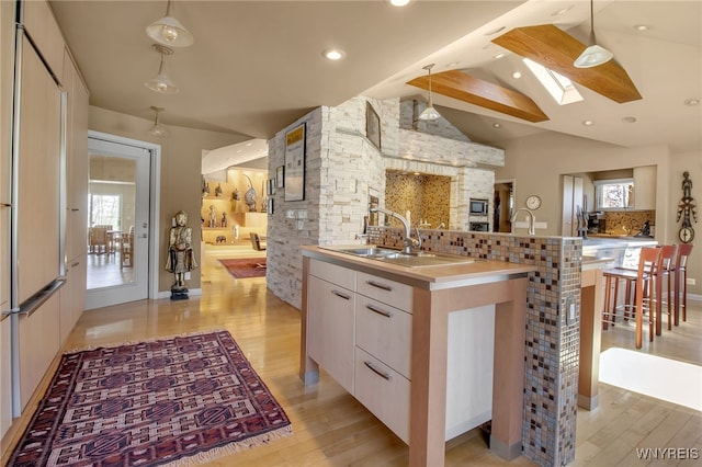 kitchen with light hardwood / wood-style flooring, white cabinetry, hanging light fixtures, vaulted ceiling with skylight, and a center island with sink