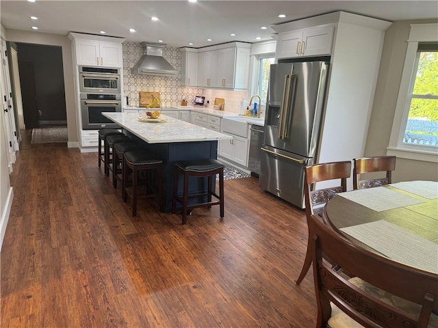 kitchen featuring white cabinets, backsplash, stainless steel appliances, dark wood-type flooring, and wall chimney exhaust hood