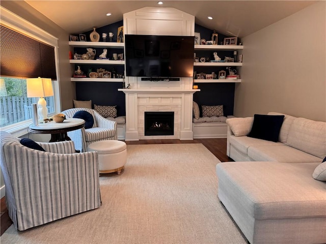 living room with lofted ceiling, a tiled fireplace, built in features, and hardwood / wood-style flooring