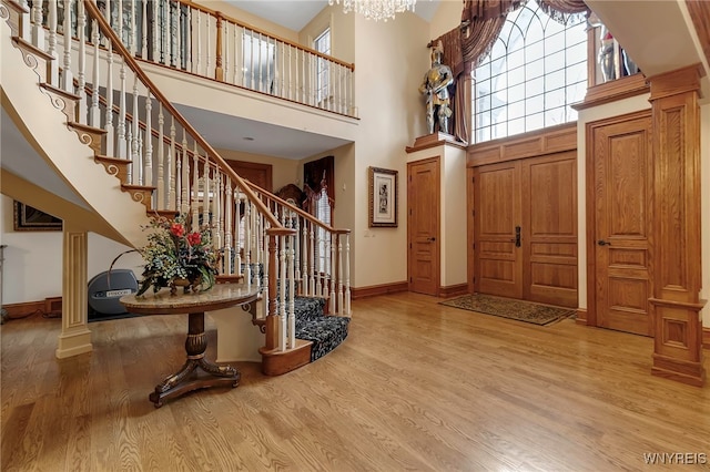 entrance foyer featuring decorative columns, a towering ceiling, an inviting chandelier, and light wood-type flooring