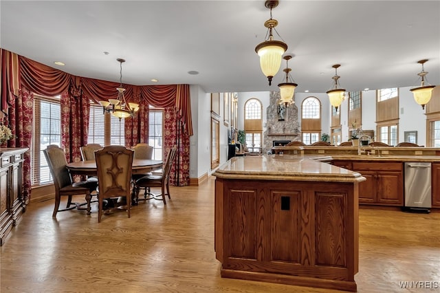 kitchen with pendant lighting, a stone fireplace, a kitchen island, and light wood-type flooring