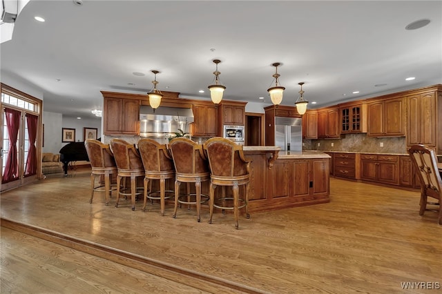 kitchen featuring a large island, built in appliances, decorative light fixtures, and light hardwood / wood-style floors