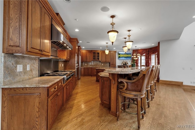 kitchen featuring hanging light fixtures, stainless steel gas cooktop, exhaust hood, light wood-type flooring, and a spacious island