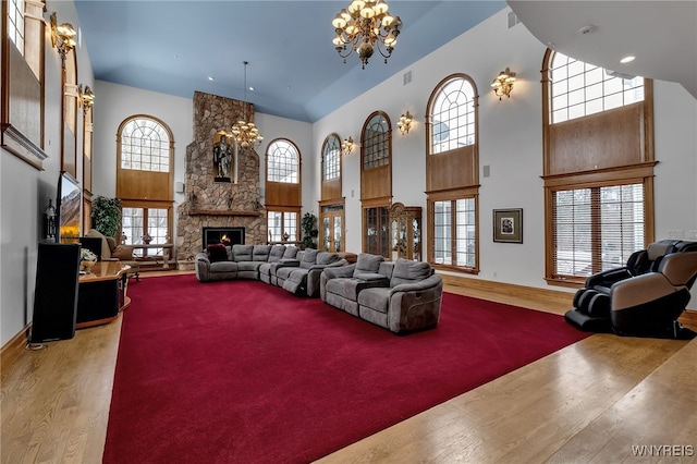 living room with a high ceiling, a stone fireplace, hardwood / wood-style floors, and an inviting chandelier