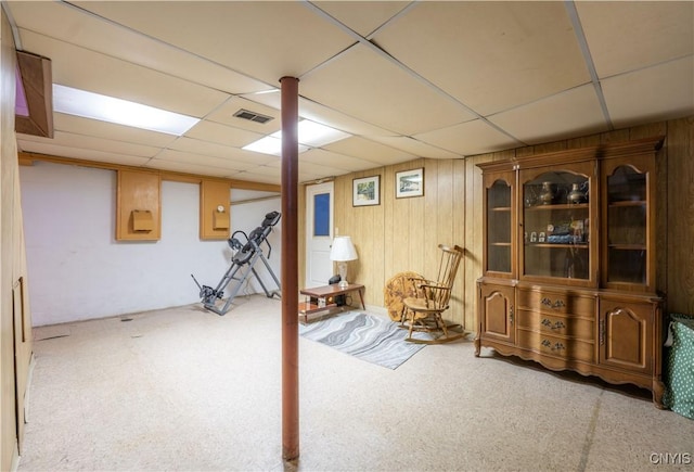 basement with light carpet, a paneled ceiling, and wood walls