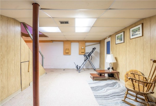 living area featuring light colored carpet, a paneled ceiling, and wood walls