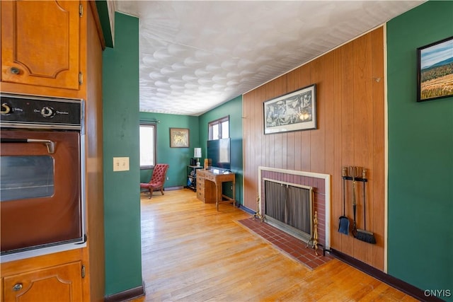 interior space featuring a brick fireplace, light hardwood / wood-style flooring, oven, and wood walls