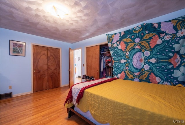 bedroom with two closets, wood-type flooring, and a textured ceiling