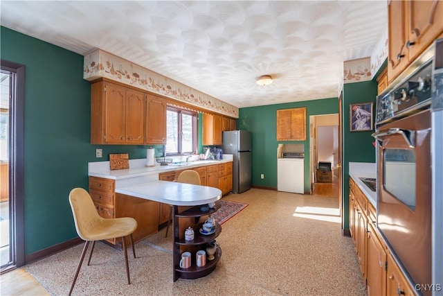 kitchen featuring sink, stainless steel refrigerator, kitchen peninsula, wall oven, and washer / clothes dryer