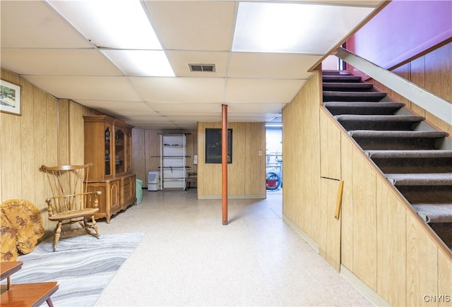 basement featuring a drop ceiling and wooden walls