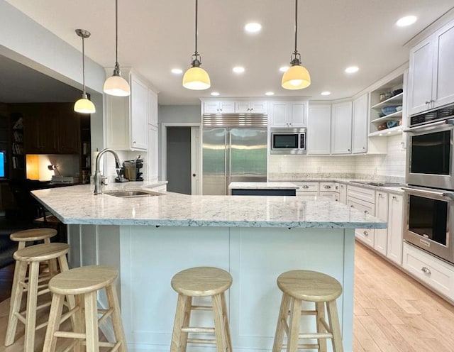 kitchen featuring built in appliances, hanging light fixtures, a breakfast bar area, light stone countertops, and sink