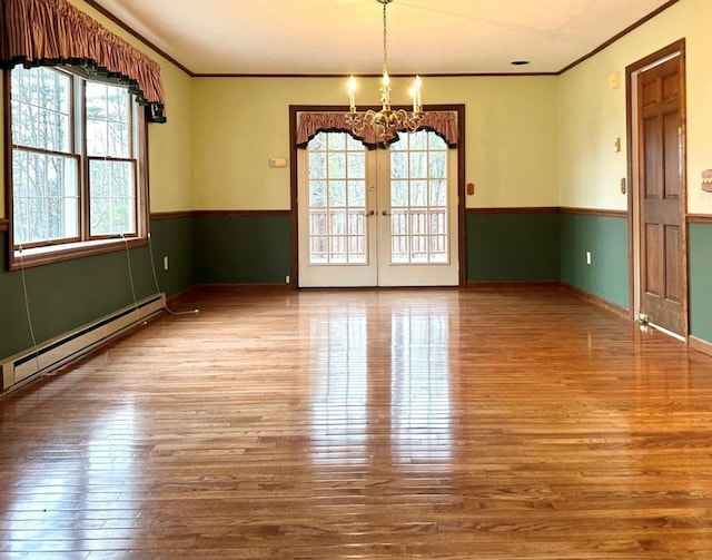 spare room with hardwood / wood-style flooring, french doors, baseboard heating, ornamental molding, and an inviting chandelier