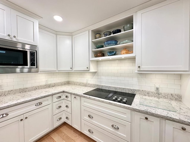 kitchen with stainless steel microwave, light stone counters, black electric stovetop, and white cabinets