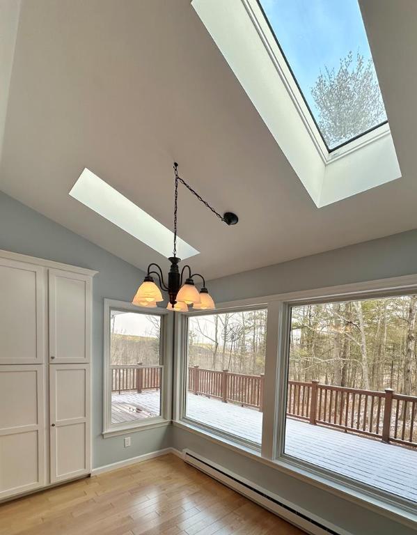 unfurnished dining area with a baseboard heating unit, a chandelier, light wood-type flooring, and vaulted ceiling with skylight