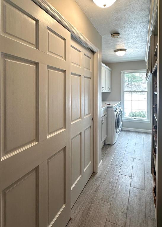 clothes washing area with light wood-type flooring, cabinets, separate washer and dryer, and a textured ceiling