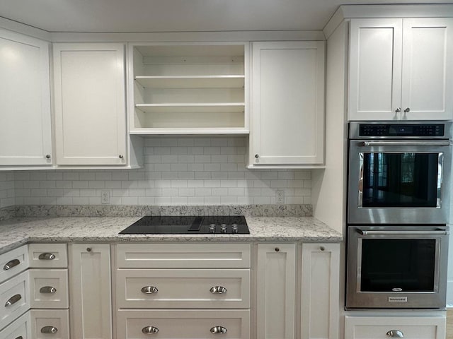 kitchen with black electric stovetop, light stone counters, white cabinets, and double oven