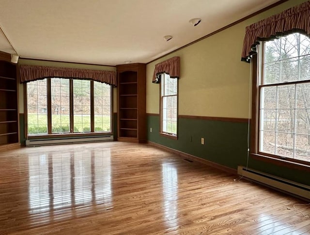 spare room featuring light wood-type flooring, crown molding, and a baseboard heating unit