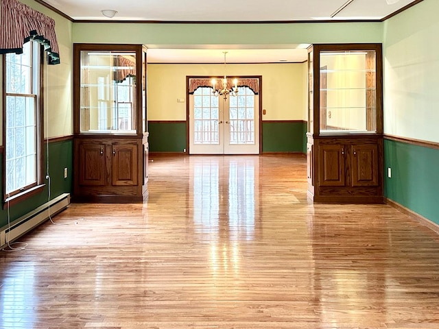 empty room with light wood-type flooring, french doors, crown molding, and a baseboard heating unit