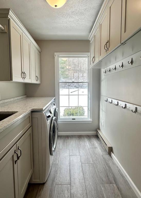 clothes washing area featuring a baseboard radiator, light wood-type flooring, a textured ceiling, washer and dryer, and cabinets