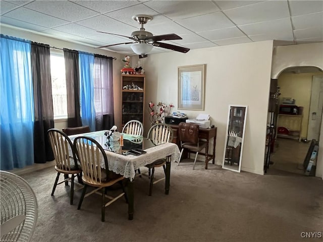 carpeted dining space with ceiling fan and a drop ceiling