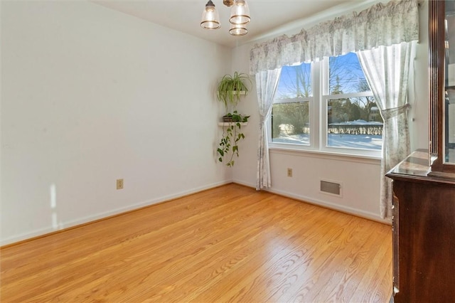 spare room with an inviting chandelier and light wood-type flooring