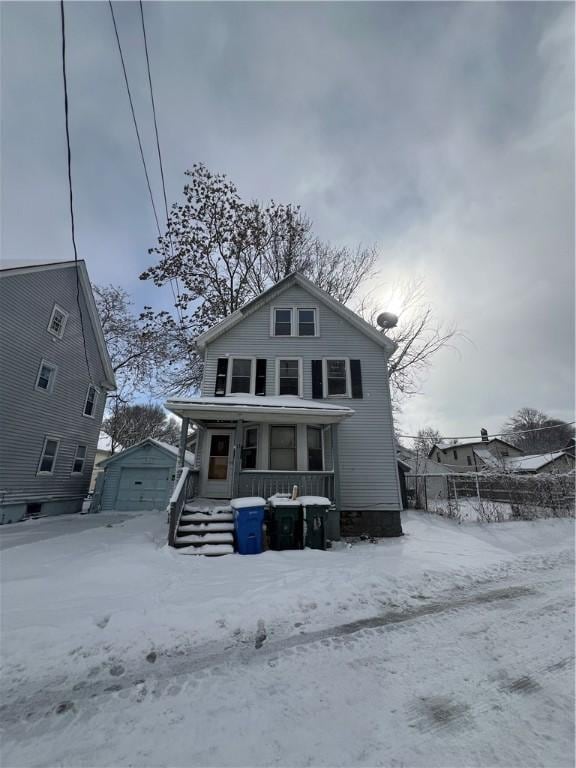 snow covered rear of property featuring an outbuilding, a garage, and covered porch