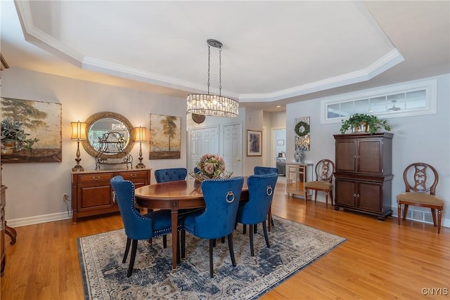 dining area featuring a raised ceiling, light hardwood / wood-style floors, a chandelier, and crown molding