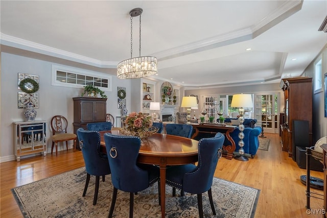 dining area featuring a raised ceiling, light hardwood / wood-style floors, a notable chandelier, and ornamental molding