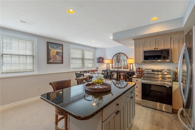 kitchen featuring a kitchen island, tasteful backsplash, appliances with stainless steel finishes, a kitchen bar, and light brown cabinetry