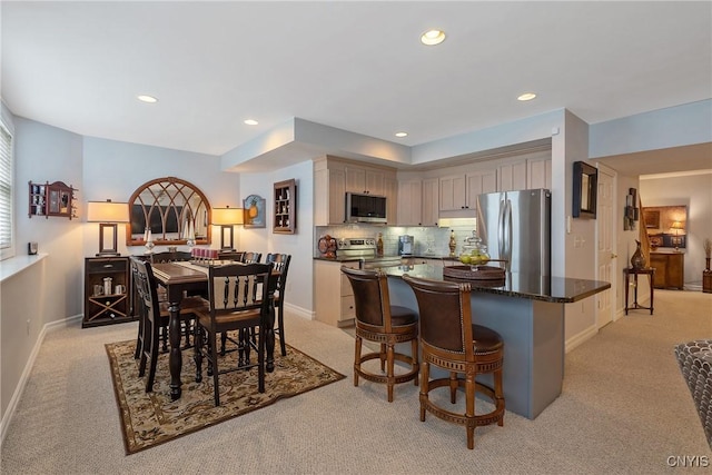 kitchen with dark stone countertops, appliances with stainless steel finishes, a kitchen island, light colored carpet, and tasteful backsplash