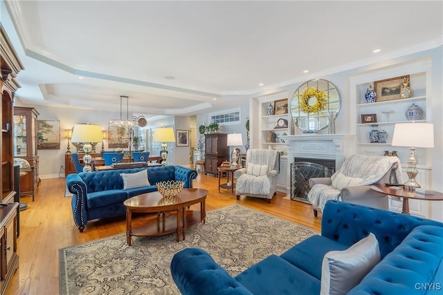 living room with light wood-type flooring, built in features, and a raised ceiling