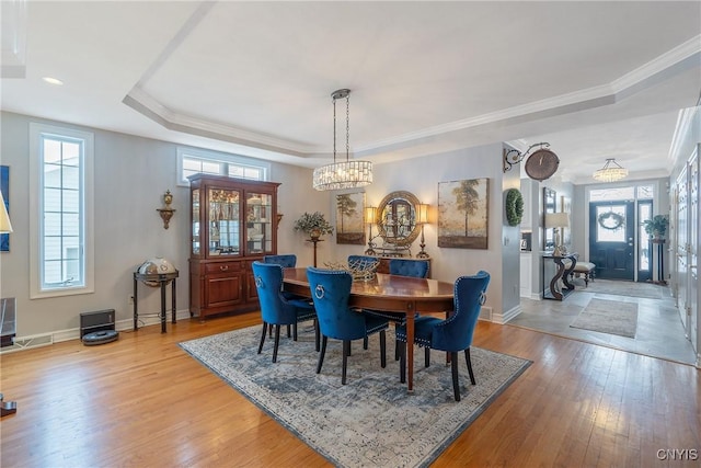 dining area with light wood-type flooring, crown molding, a chandelier, and a raised ceiling