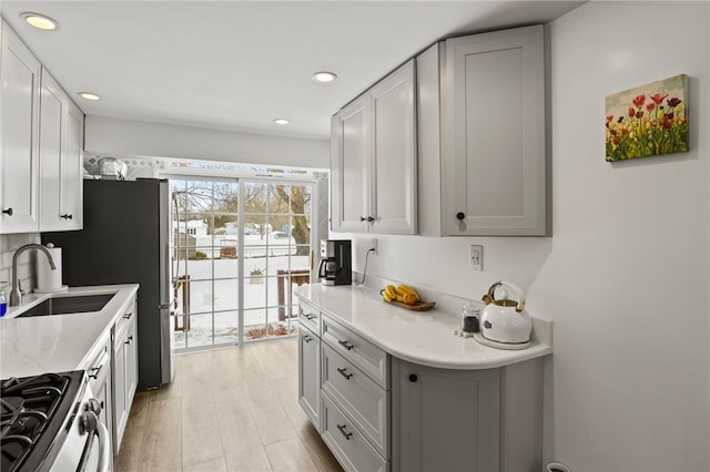 kitchen featuring light hardwood / wood-style floors, stainless steel range oven, light stone countertops, and sink