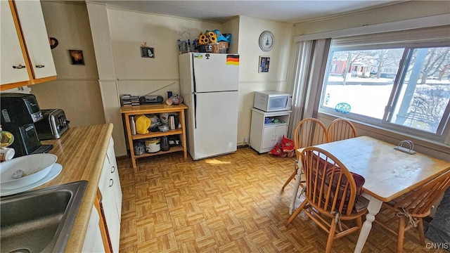 kitchen with white cabinetry, sink, white appliances, and light parquet flooring