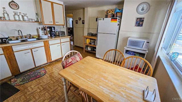 kitchen with light parquet floors, white cabinetry, sink, and white appliances