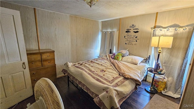 bedroom with dark hardwood / wood-style floors, wooden walls, and a textured ceiling