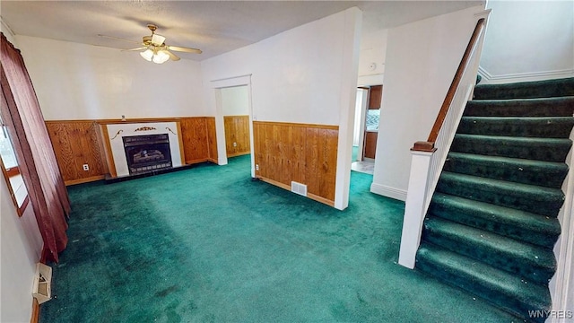 unfurnished living room with ceiling fan, wooden walls, and dark colored carpet