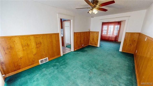 unfurnished room with ceiling fan, a textured ceiling, dark carpet, and wood walls